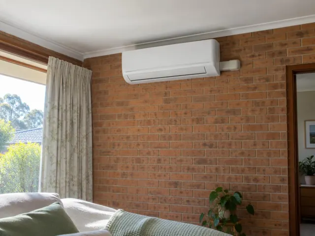 Wall-mounted split system on a brick feature wall in a living room with window curtains in Flagstaff Hill